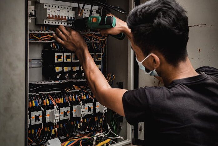 Technician working on circuit breaker panel, adjusting electrical wires indoors.